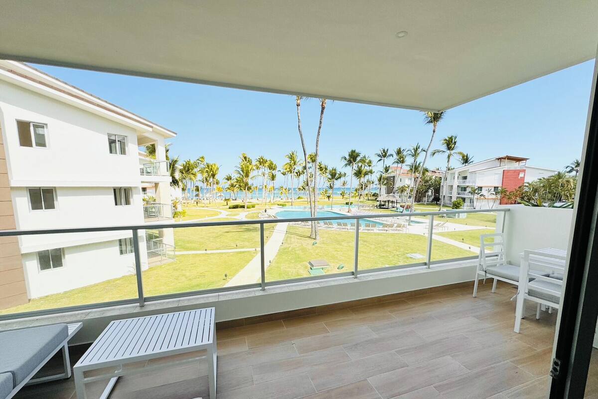 A balcony with a view of a pool, palm trees, and a building complex.