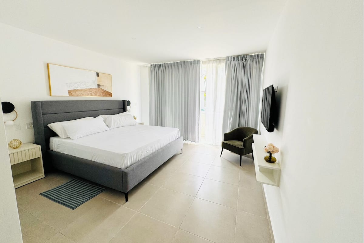 A modern hotel room with a large bed, a desk, a chair, and a TV mounted on the wall.