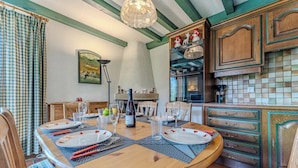 A dining area with a wooden table set for four, surrounded by chairs. A chandelier hangs from the ceiling, and there is a kitchen area with wooden cabinets and a tiled backsplash. - Comfort with Balcony and parking (Val Thorens)
