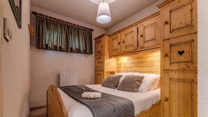 A bedroom with a wooden bed, a bedside table, a nightstand, a window with curtains, and wooden paneling on the walls. - Comfort with Balcony and parking (Val Thorens)
