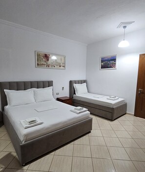 A hotel room with two beds, a nightstand, a wooden door, and two framed pictures on the walls. - Vila Malo (Ksamil)