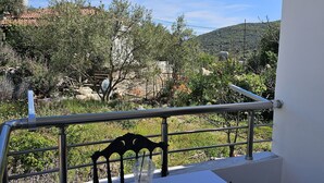 A balcony with a table and chairs, overlooking a mountainous landscape with trees and a clear sky. - Vila Malo (Ksamil)