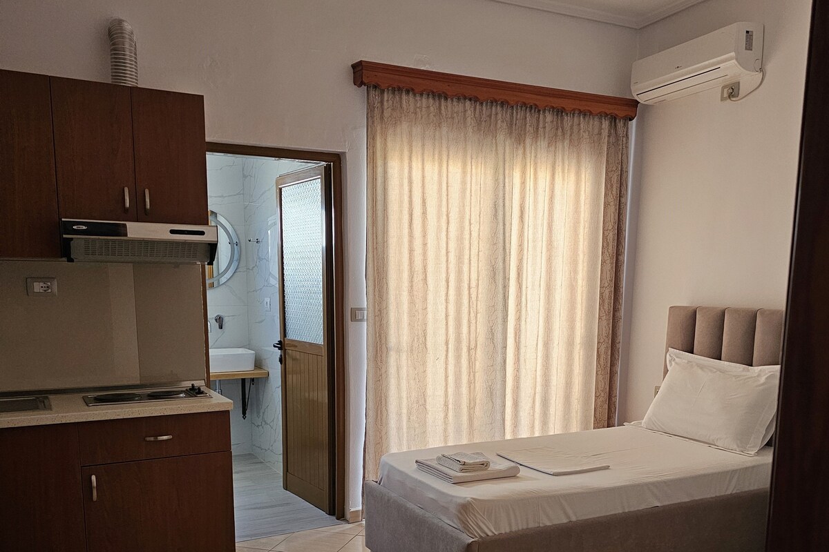 A room with a bed, a small sofa, a kitchenette, and a bathroom visible through an open door.