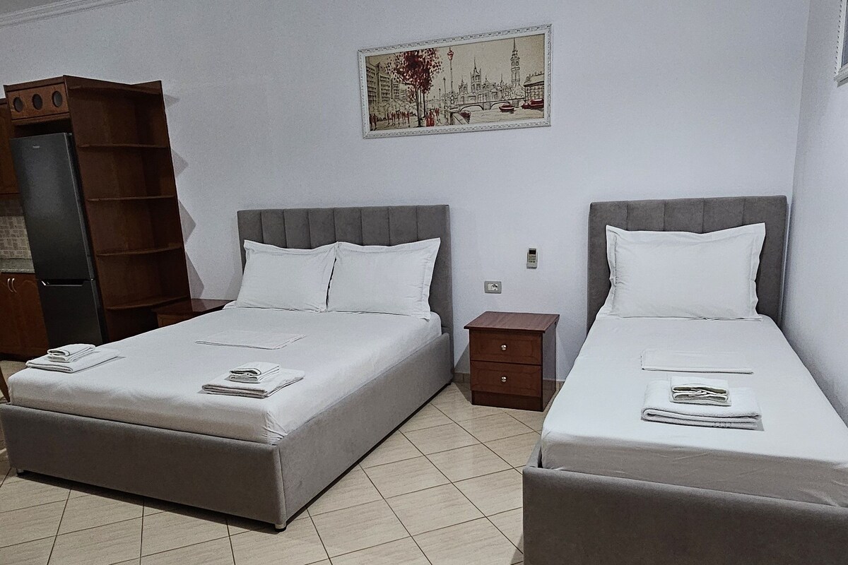 A hotel room with two beds, a small bedside table, a wardrobe, and a painting on the wall.