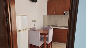 A compact kitchen with wooden cabinets, a built-in microwave, and a small dining table with chairs. - Vila Malo (Ksamil)