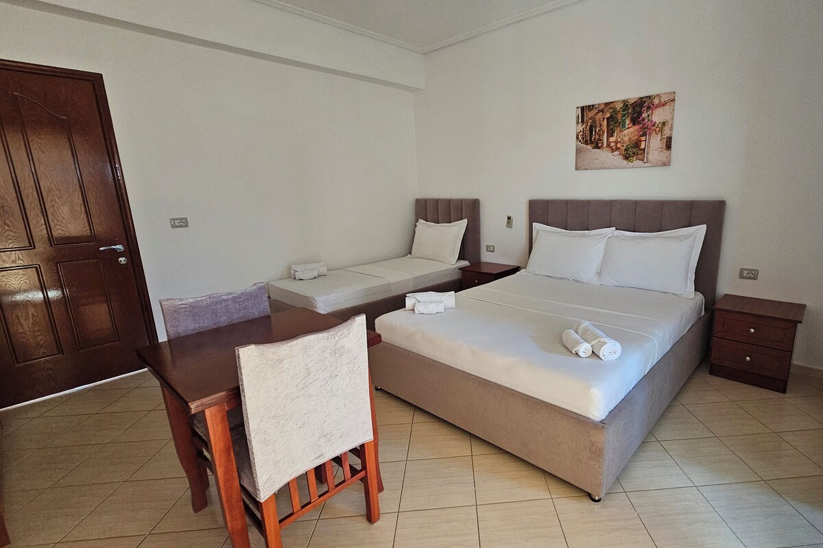 A hotel room with a large bed, a smaller bed, a desk, and a chair.