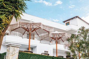 Ein weißes Gebäude mit Balkon, Sonnenschirmen und einer Palme.