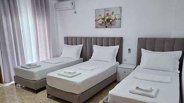 A hotel room with three beds, a ceiling fan, an air conditioning unit, and a painting on the wall. - Vila Malo (Ksamil)