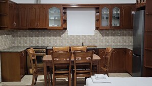 A compact kitchen with wooden cabinets, a dining table with chairs, and a refrigerator. - Vila Malo (Ksamil)
