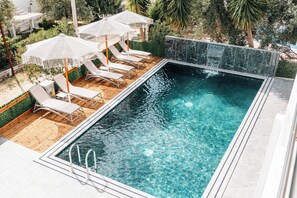 A rectangular swimming pool with clear water, surrounded by wooden decking and white lounge chairs with umbrellas. - Vila Malo (Ksamil)