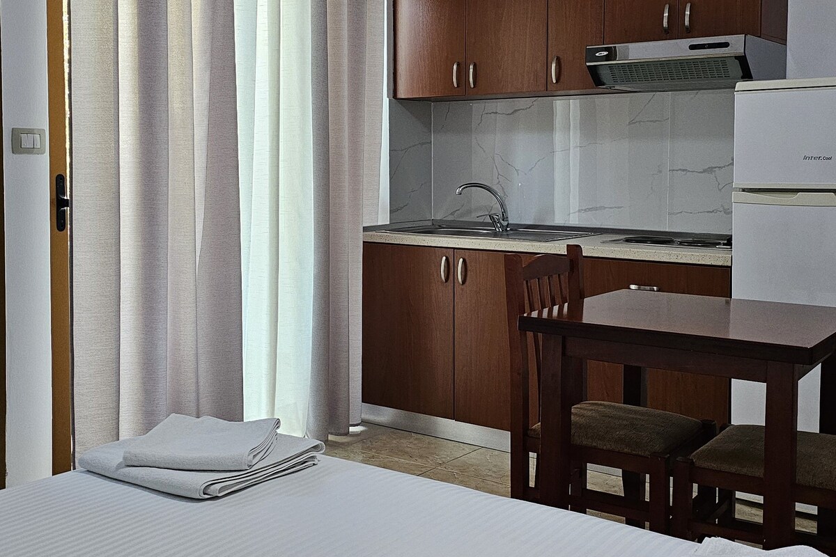 A compact hotel room with a bed, a small kitchenette, a dining area, and a bathroom.