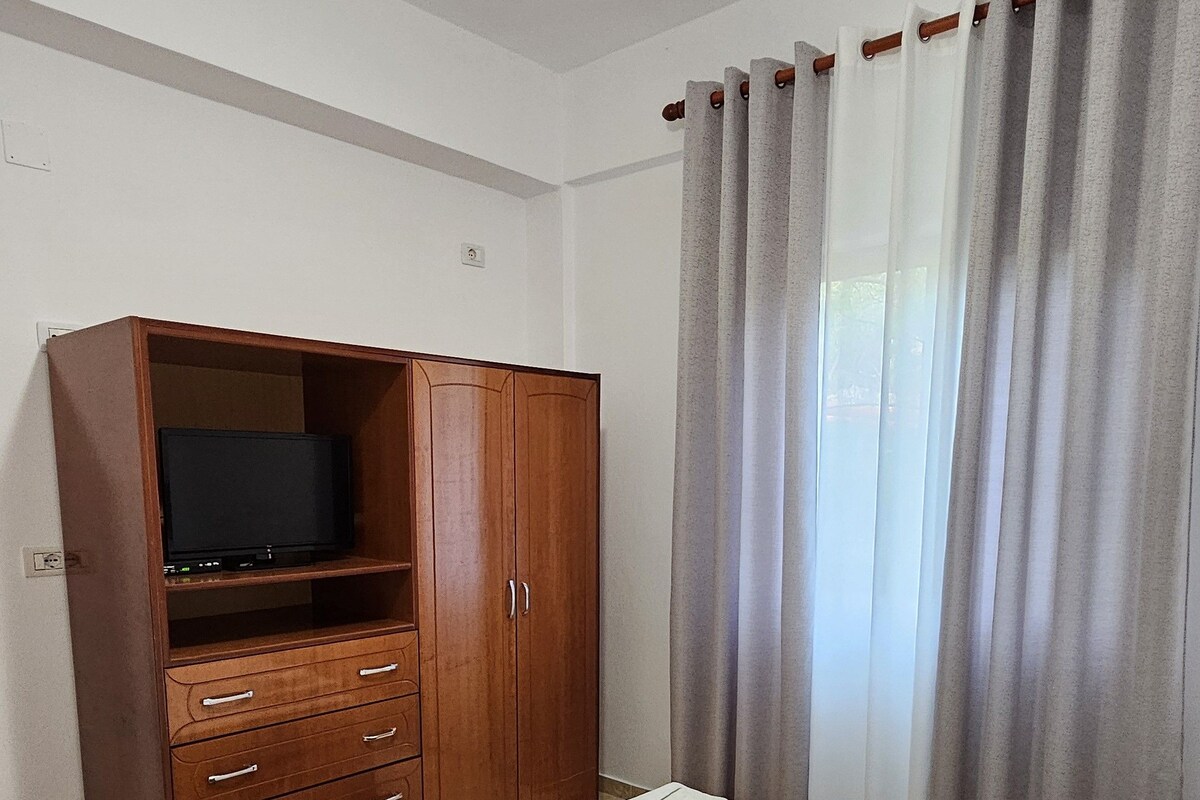 A bedroom with a bed, a wooden wardrobe, a television, and a curtain.