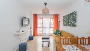 Ein modernes Wohnzimmer mit einer Couch, einem Couchtisch, einem an der Wand befestigten Fernseher und einem Fenster mit Vorhängen.