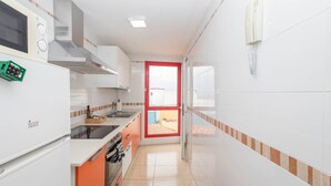 Eine kleine Küche mit weißen Schränken, einer türrot gerahmten Tür und Blick auf einen Balkon.