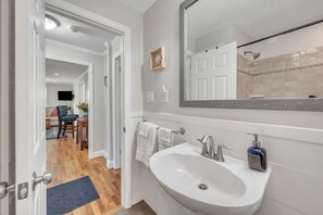 A modern bathroom with a large mirror, white sink, and a shower area.