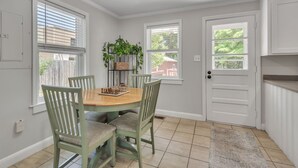 A dining area with a round table, four chairs, and a plant on a stand. - The Oleander Cottage (Wilmington)