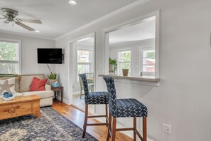 A living room with a sofa, coffee table, TV, and two patterned chairs. - The Oleander Cottage (Wilmington)