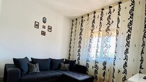 Ein modernes Wohnzimmer mit einem schwarzen Ecksofa, Holzdielenboden und gemusterten Vorhängen.