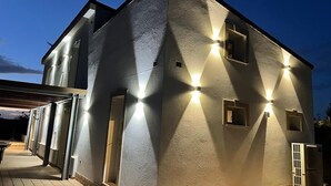 Een modern gebouw met buitenverlichting, een overdekt terras met tafels en een gevel van baksteen.