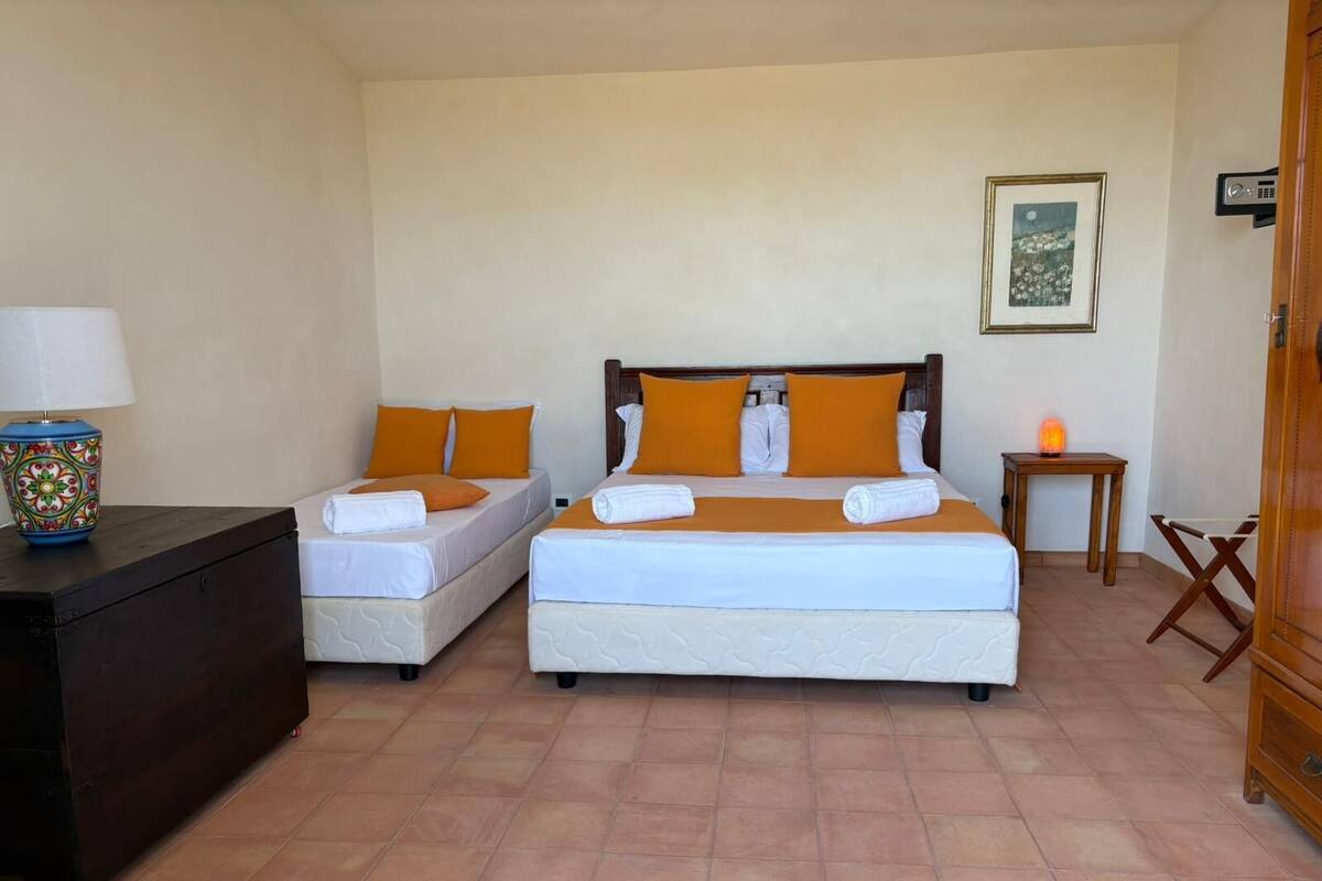 A hotel room with two beds, a wooden dresser, a lamp, and a small table with a heater.
