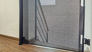 A black metal gate with a fine mesh, attached to a wall with a white baseboard.