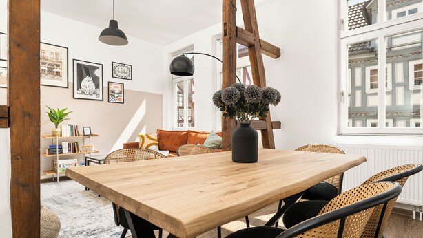 A dining area with a wooden table, wicker chairs, and a vase of flowers.