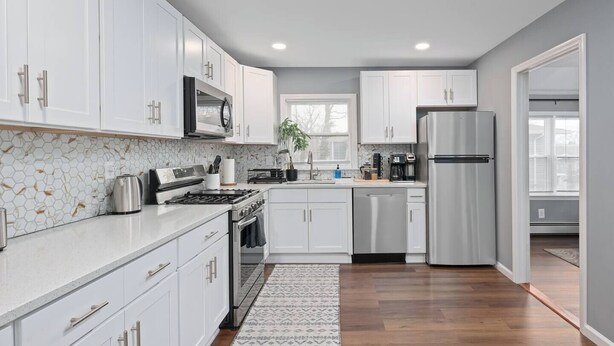 A modern kitchen with white cabinets, stainless steel appliances, and a patterned backsplash. - Cozy Home, 17 min from NYC, 2 Parking Spaces (Ridgefield Park)