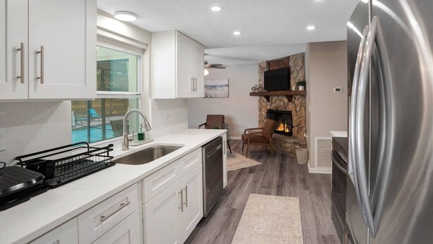 A modern kitchen with white cabinets, a stainless steel refrigerator, a stone fireplace, and a view of a pool. - Cozy Pool House 24 min to Beach, Cozy Pool House 24 min to Beach (Manatee County)