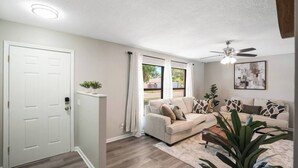 A living room with a beige sofa, a ceiling fan, and a large window with curtains. - Cozy Pool House 24 min to Beach, Cozy Pool House 24 min to Beach (Manatee County)