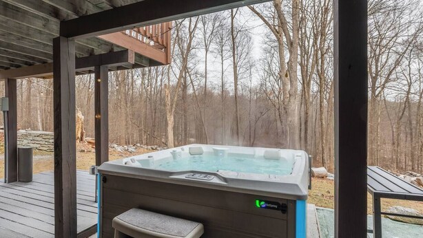 Ein Whirlpool in einem überdachten Außenbereich mit einer Holzterrasse und Blick auf einen Wald.