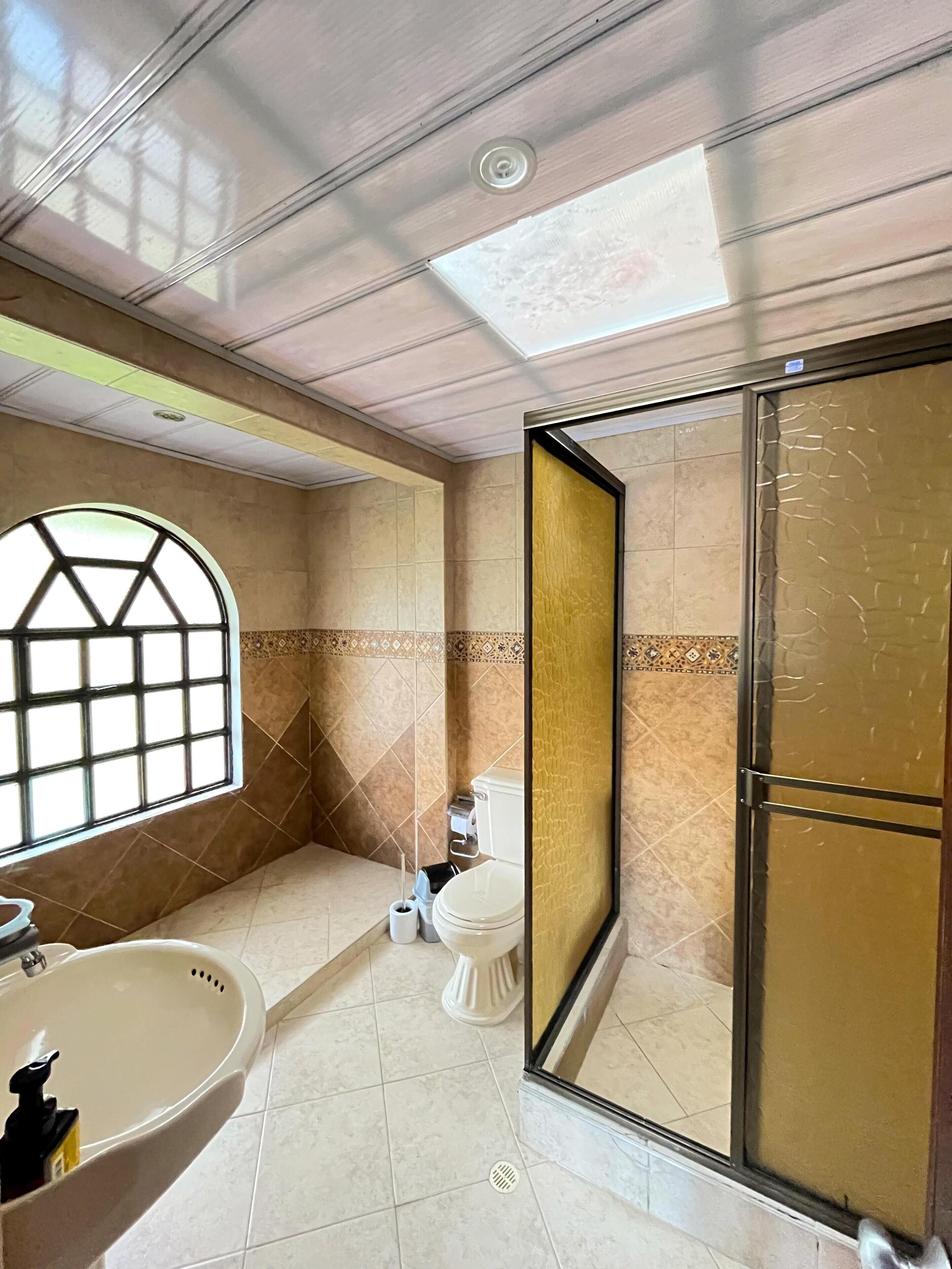 A bathroom with a large window, a sink, a toilet, and a shower area.