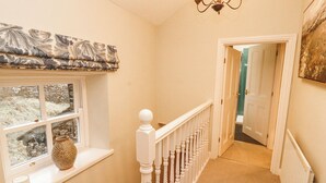 A hallway with a white railing, a window with a view, and a door leading to another room. - Deer How Farm (Penrith)