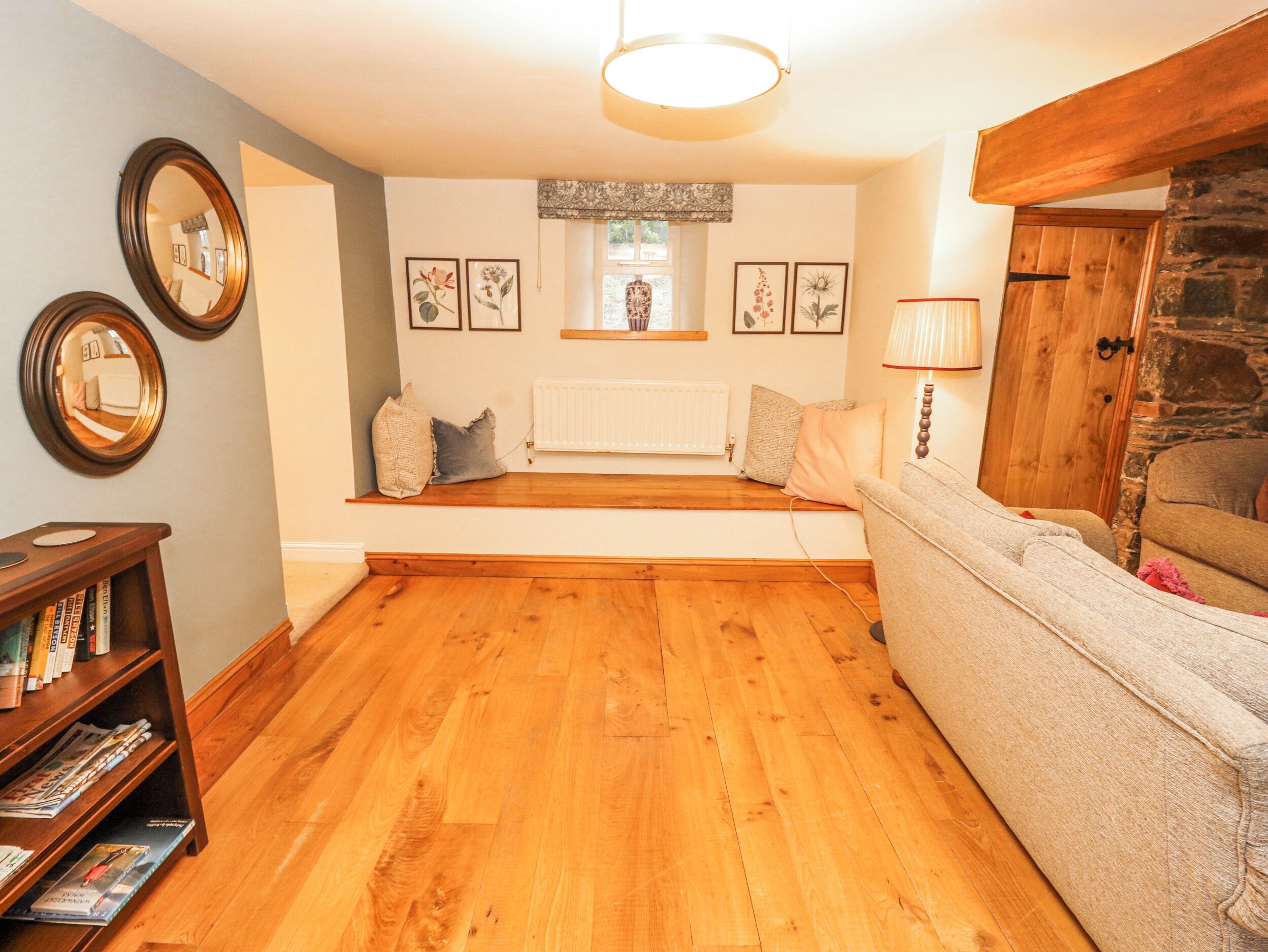 A cozy living room with a wooden floor, a sofa, a bookshelf, and a fireplace.