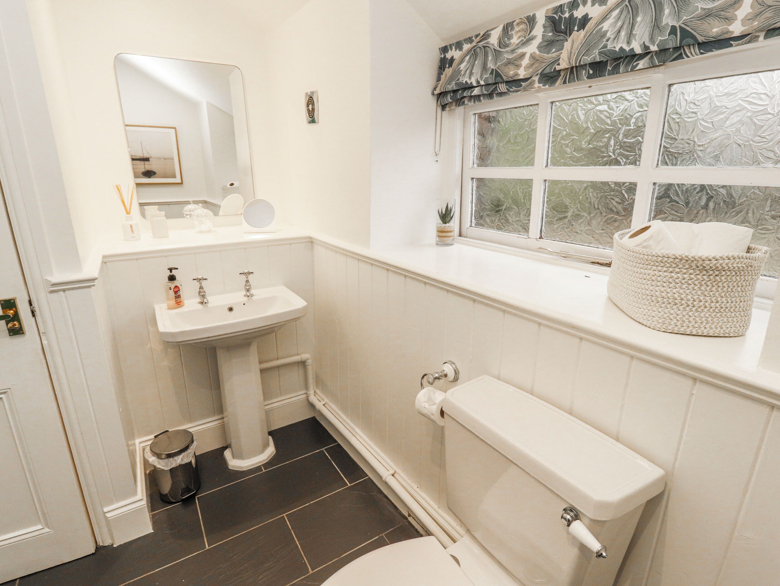 A bathroom with a pedestal sink, toilet, and a window with a view of trees.