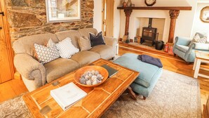 A cozy living room with a stone wall, a fireplace, a sofa, a coffee table, and a blue armchair. - Deer How Farm (Penrith)