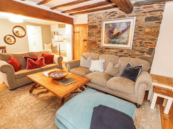 Un salón acogedor con pared de piedra, techo de madera y un cuadro. Hay un sofá con cojines y una mesa de centro con un cuenco y un libro.