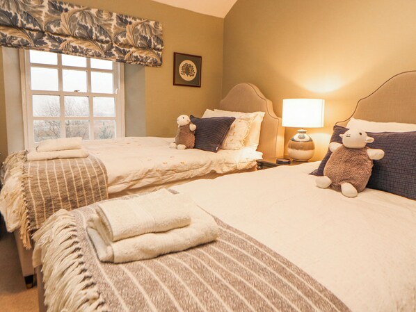 A hotel room with two beds, a window with a view, a lamp, and a framed picture on the wall. - Deer How Farm (Penrith)