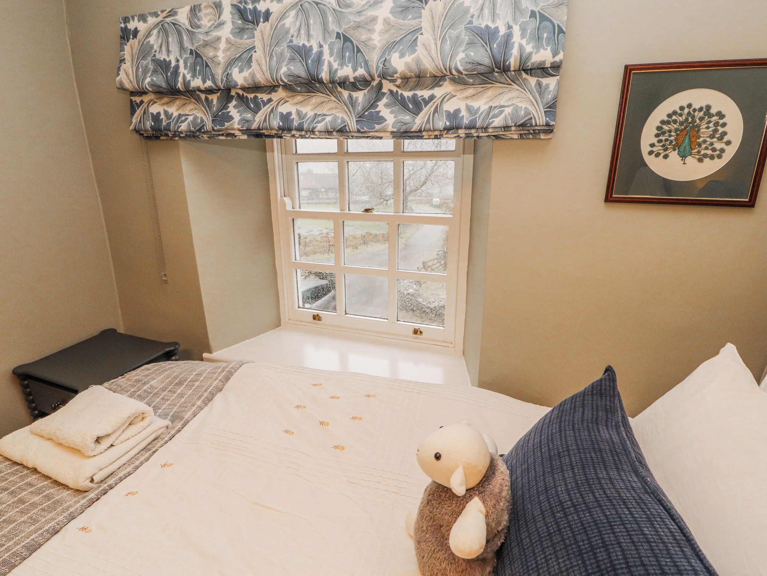 Un dormitorio con cama, ventana, un cuadro enmarco y una mesita.