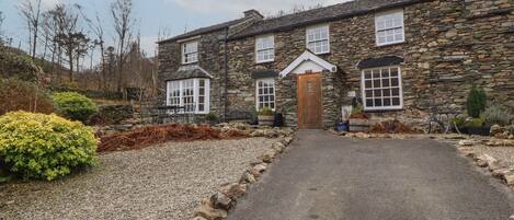 A stone house with a gravel driveway leading to a wooden door.