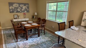 A dining area with a wooden table set for four, surrounded by chairs, a patterned rug, and a window with a view of greenery. - Perfect 3 bed 2 bath football weekend house. 10 minute walk to the square. (Oxford)