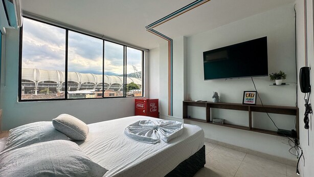 Ein Schlafzimmer mit großem Fenster, einem Bett, einem Fernseher und einem Regal mit Pflanze und Schild.