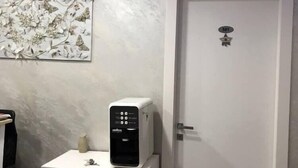 A hotel room with a white dresser, a water dispenser, a wall-mounted light fixture, and a door with a number plate. - Rome Point Inn (Rome)