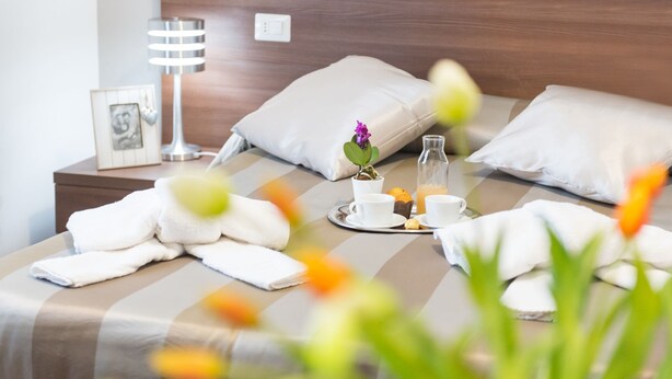 A neatly made bed with white towels, a small potted plant, and a tray with cups and a bottle. - Rome Point Inn (Rome)