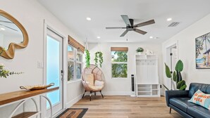 Una sala de estar moderna con piso de madera, un ventilador de techo, un sofá con cojín, una silla colgante y un ventanal con vistas a zonas verdes.