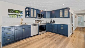 Una cocina moderna con armarios azul oscuro, electrodomésticos de acero inoxidable y encimera blanca.