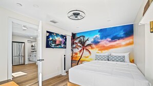 Un dormitorio moderno con una cama grande, un mural de atardecer vibrante y una cocina al fondo.