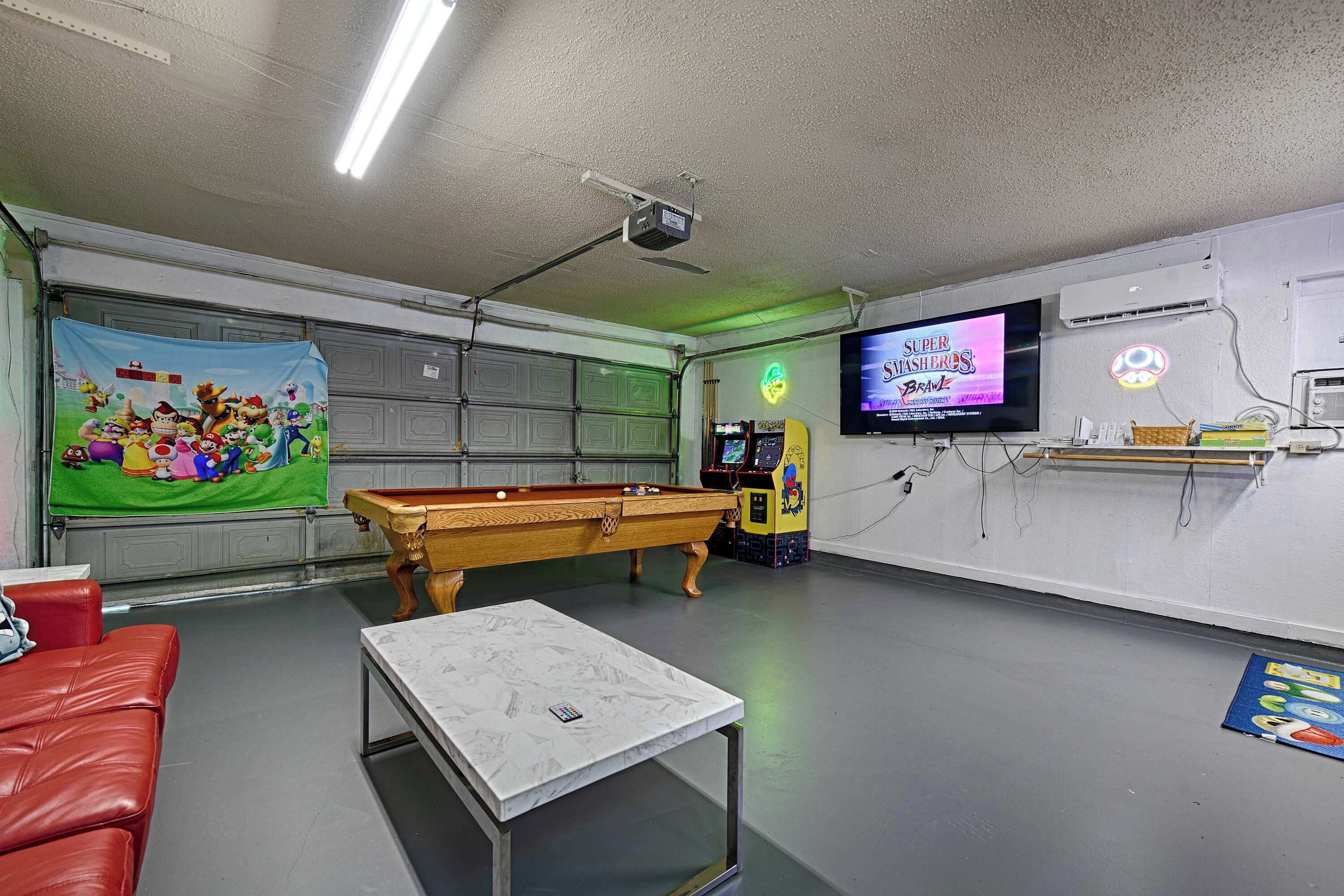 A room with a pool table, a red couch, a projector, a TV, and arcade games.
