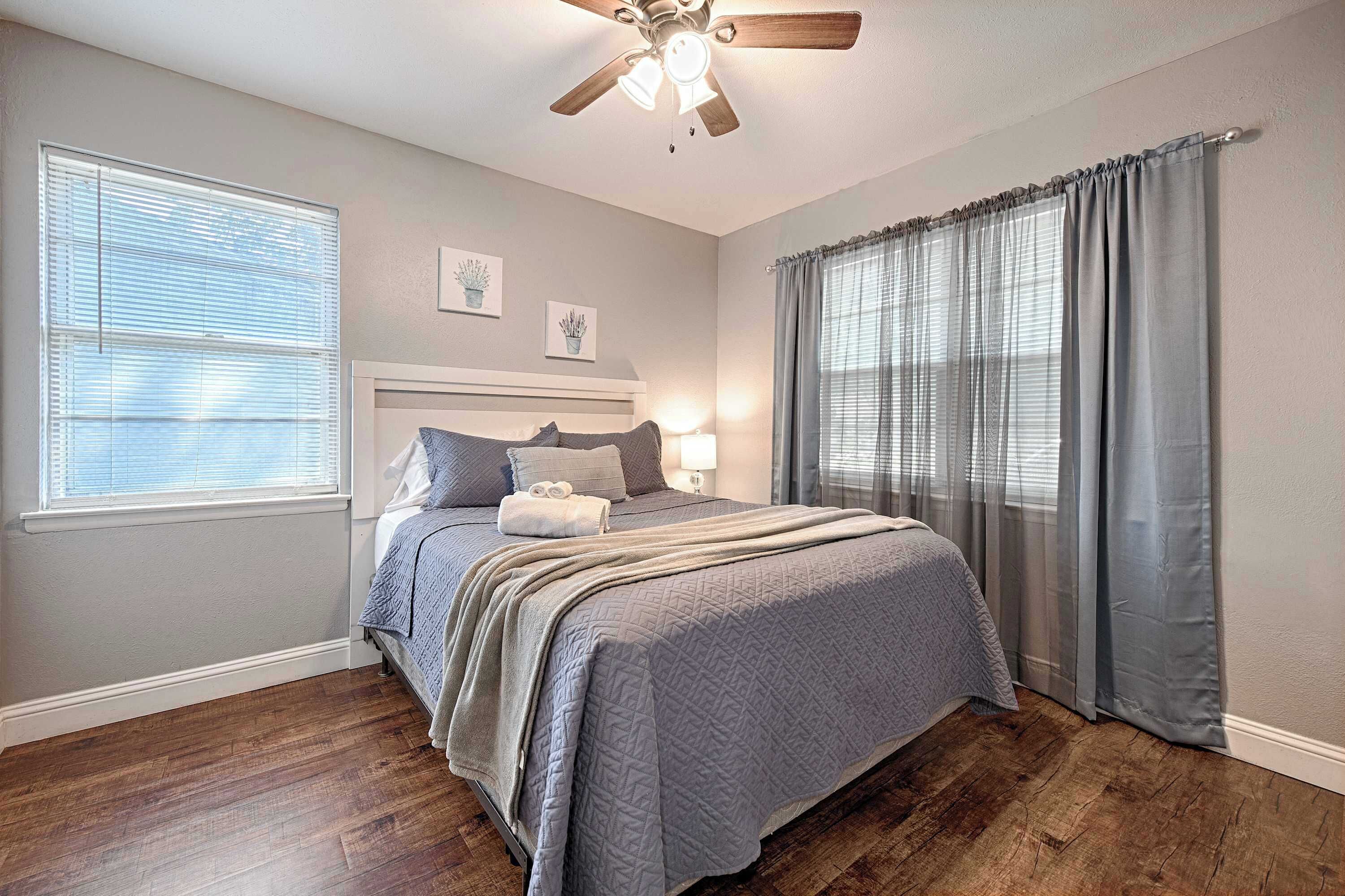 A bedroom with a bed, a ceiling fan, a window with blinds, and a curtain.