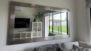 A living room with a large mirror, a flat-screen TV, and a white shelving unit. - First Floor*Coto*Pool*AC*TV*WiFi*10 min to Bucerías* (Aldea Hortus)