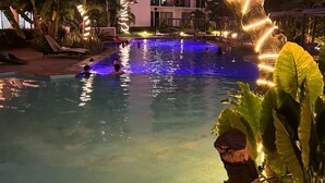 A swimming pool with illuminated edges, surrounded by palm trees and a multi-story building with balconies. - First Floor*Coto*Pool*AC*TV*WiFi*10 min to Bucerías* (Aldea Hortus)